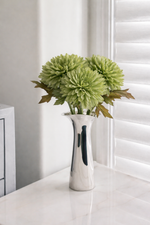 Silver vase with green flowers on a white surface