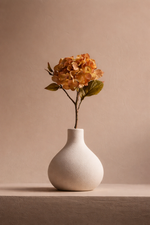 White vase with a single stem of orange flowers on a beige background