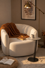Cozy living room with a white armchair, brown blanket, book, and coffee cup.