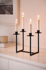 Four lit candles in black candle holders on a light surface with a neutral background