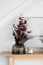 Decorative vase with red branches on a wooden table against a white wall.