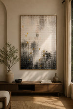 A large vertical abstract wall art piece with a textured, scale-like pattern in cream, gray, black, and small gold accents, displayed in a warm, modern living room setting above a wooden console table.