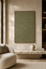 A framed abstract wall art piece with flowing contour-line patterns in muted sage green and cream, displayed in a modern living room setting above a stone console table.