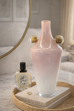 Pink vase with gold accents on a tray with a book and perfume bottle.