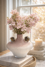Decorative vase with pink flowers on a table near a window