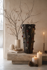 Decorative vase with geometric patterns on a wooden surface with candles and branches.