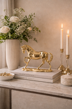Gold horse statue on books with a vase of flowers and candles in the background