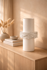 White ceramic vase with ruffled design on a wooden surface with soft lighting