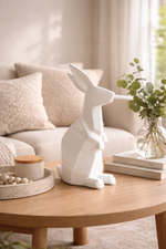 White ceramic rabbit sculpture on a wooden coffee table with a cozy living room background.