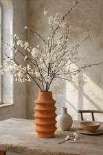 Terracotta vase with white flowers on a wooden table against a textured wall.