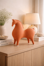 Terracotta horse sculpture on a wooden surface with a lamp and books in the background.