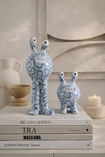 Two blue ceramic figures on top of books with a neutral background