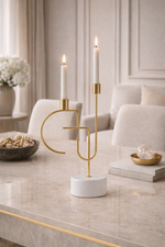 Gold candle holder with two lit candles on a marble surface in a stylish room.