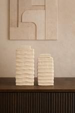Two textured ceramic vases on a wooden surface with a neutral wall in the background