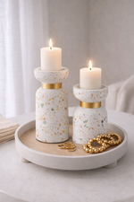 Two terrazzo-patterned candle holders with gold bands on a white tray, featuring lit candles.