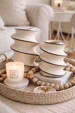 Decorative setting with candles, books, and ceramic vases on a woven tray.