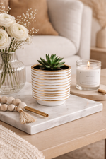 Decorative setting with a potted plant, candle, and flowers on a marble tray.