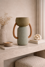 Ceramic vase with wooden handles on a table with decorative items.