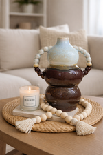 Decorative ceramic piece with beads and a candle on a wooden table in a living room setting.