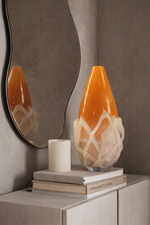Decorative orange and white vase on books with a mirror reflection in a neutral setting