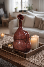 Decorative red ceramic vase on a wooden tray with candles in a living room setting.