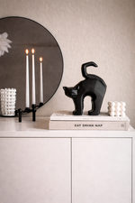 Black cat sculpture on a book with candles and a mirror in the background