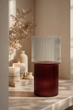 Decorative glass vase with ribbed design on a wooden surface with candles and flowers.