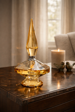 Decorative amber glass bottle on a wooden surface with a candle and birds in the background.
