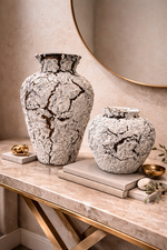 Two textured vases on a marble surface with a round mirror in the background.
