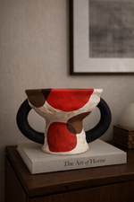 Ceramic vase with red, black, and beige design on a wooden surface with 'The Art of Home' book.