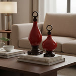 Two red decorative bottles on books with a beige sofa and lamp in the background