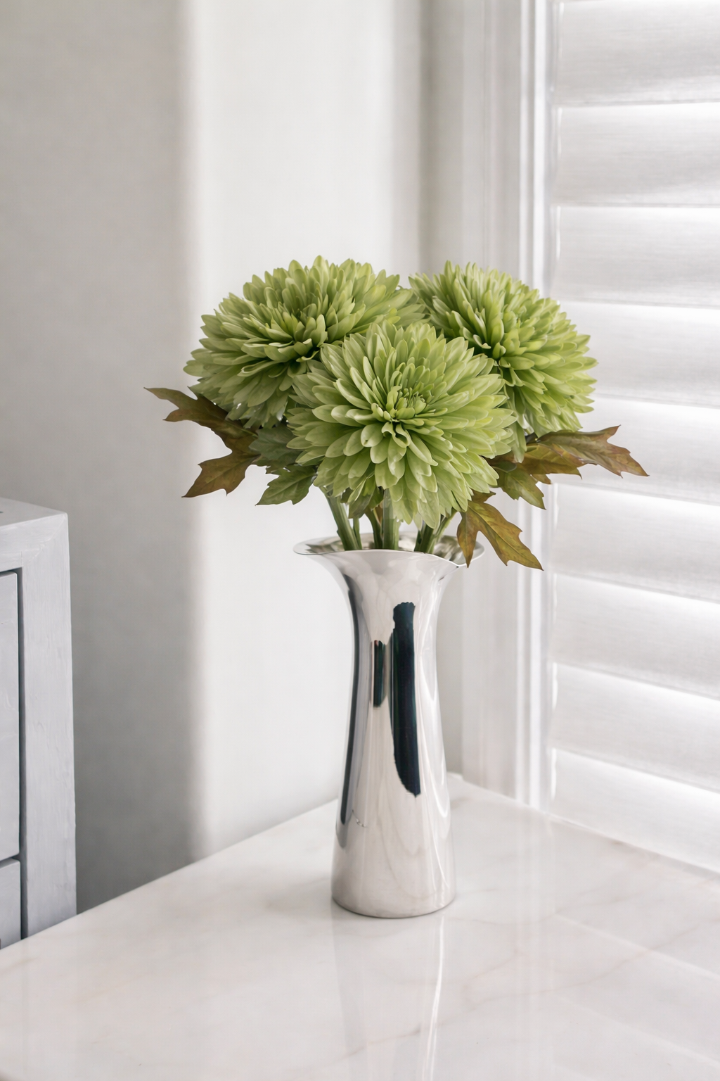 Silver vase with green flowers on a white surface