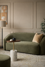 Green sofa in a room with a lamp, side table, and wall art.