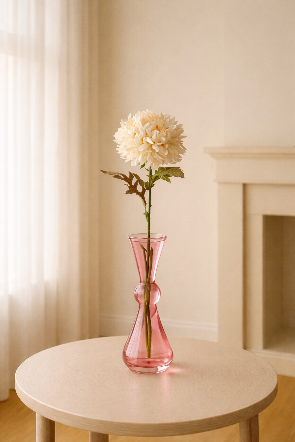Pink vase with a white flower on a round wooden table against a neutral wall.