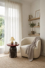 Cozy living room with a white armchair, small table, and shelves with decor items.