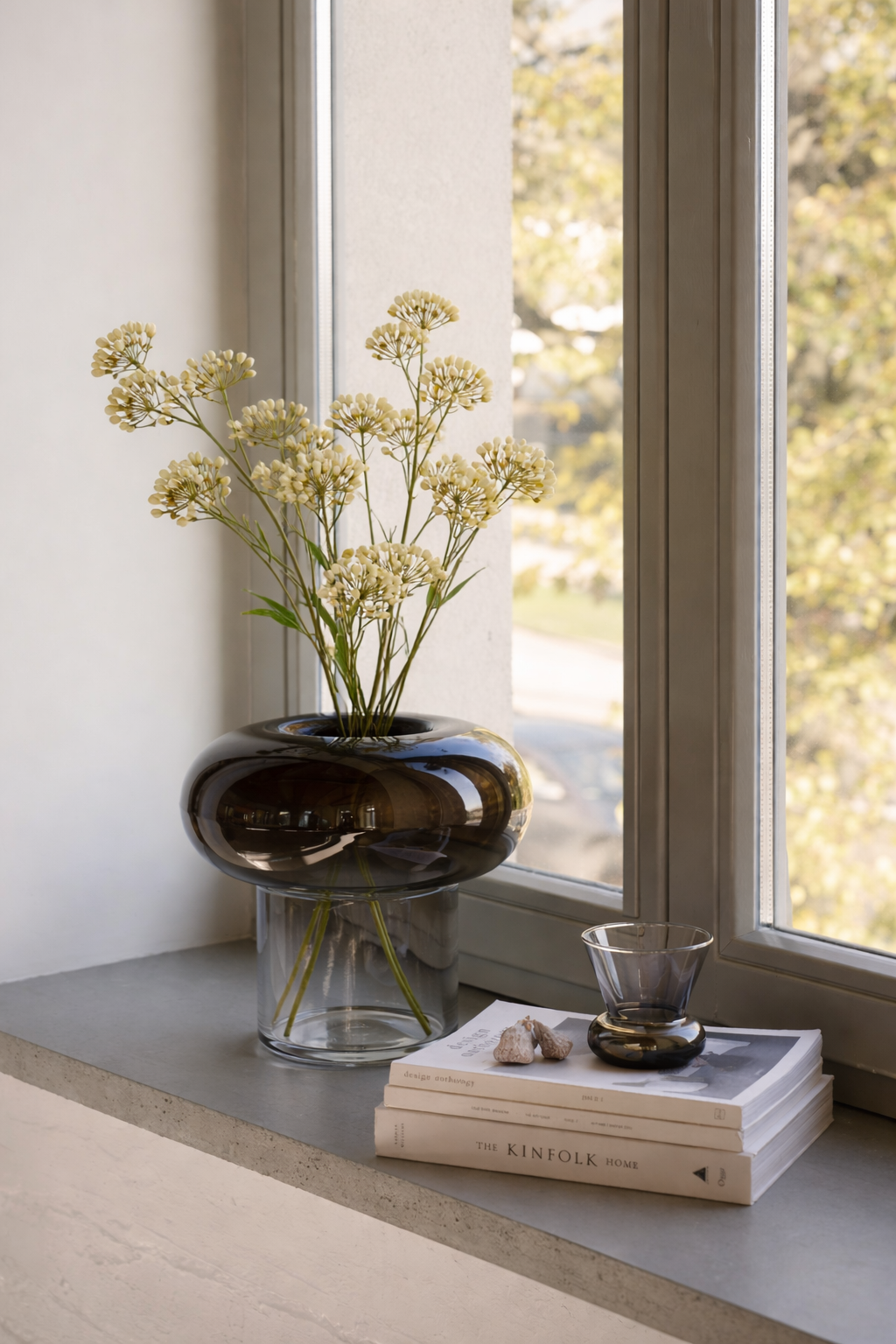 Decorative vase with flowers on a windowsill next to books and a glass.