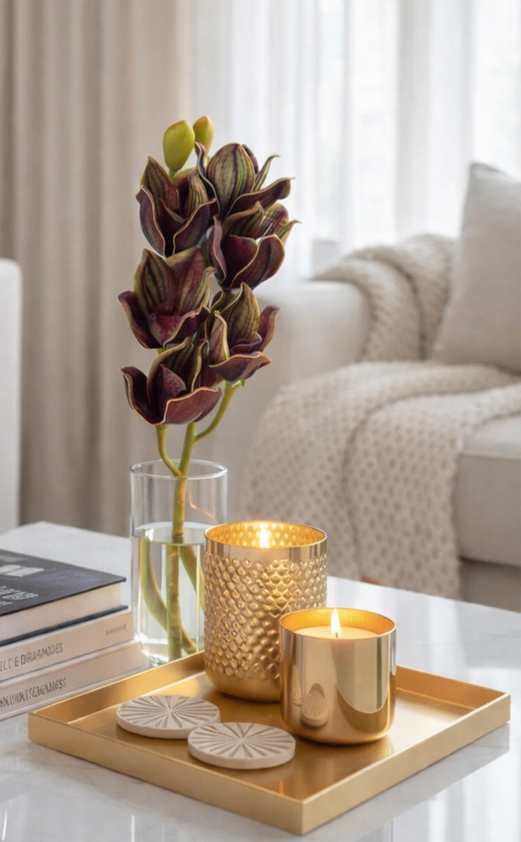 Decorative setup with gold candle holders, a vase with flowers, and books on a tray in a living room.
