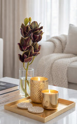 Decorative setup with gold candle holders, a vase with flowers, and books on a tray in a living room.