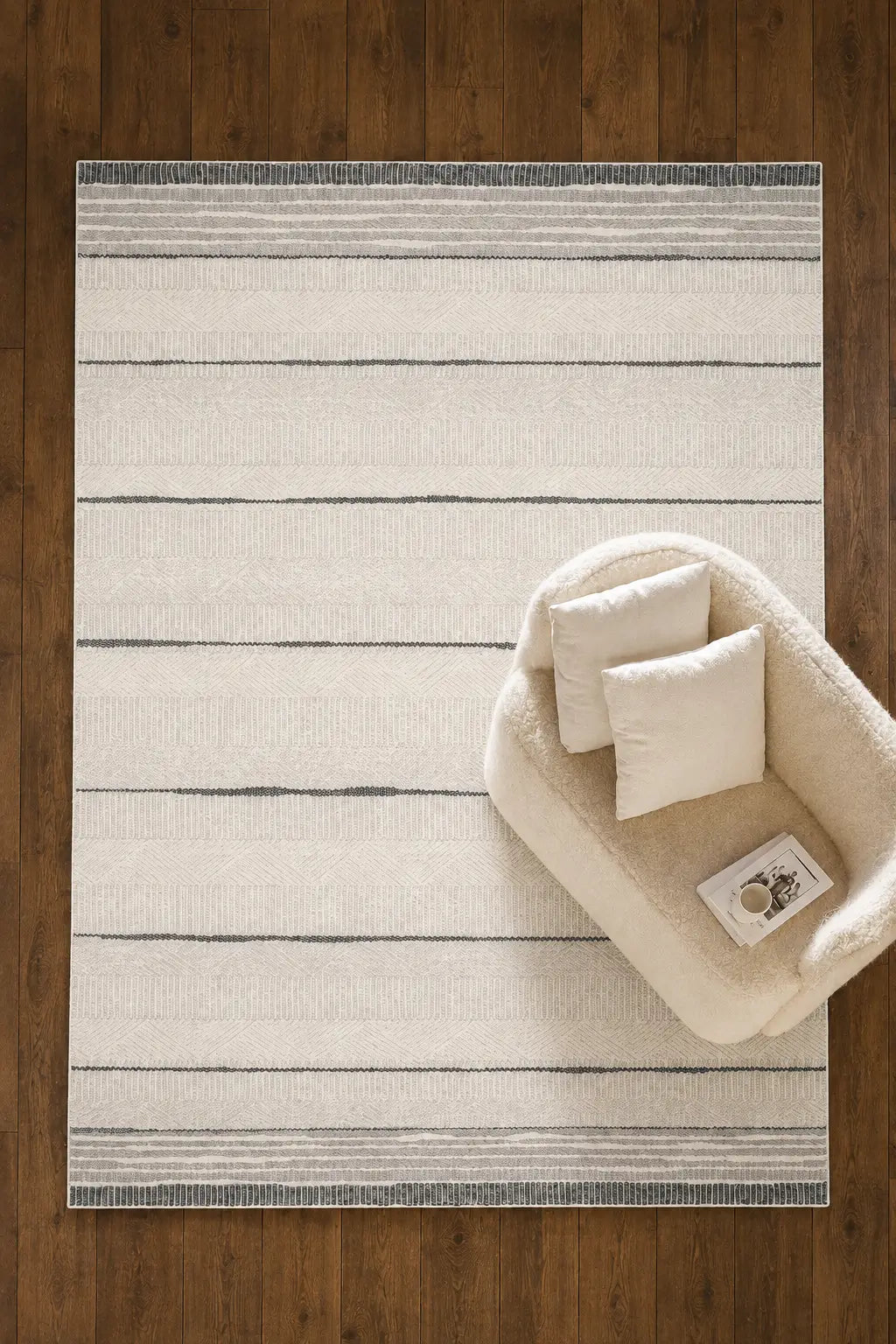 A rectangular cream and gray striped area rug laid on a dark wood floor, styled with a small cream upholstered accent chair and two matching pillows.