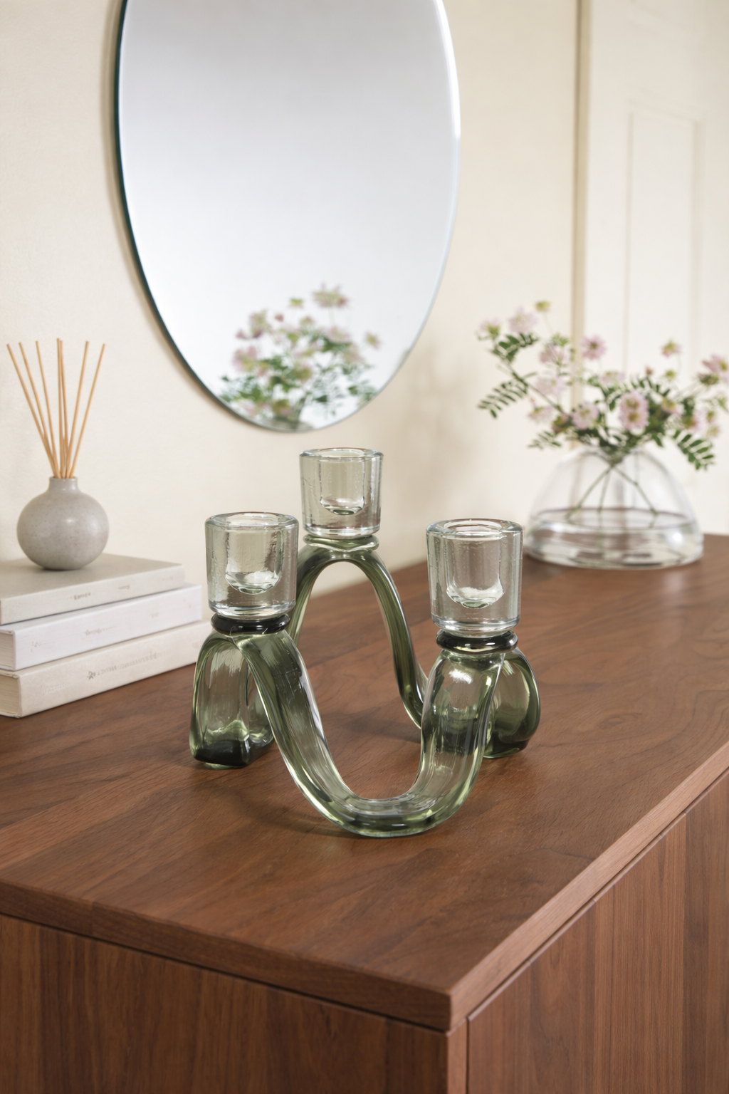 Decorative glass candle holder on a wooden surface with a mirror and flowers in the background