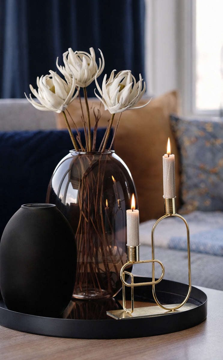 Decorative setup with a vase of white flowers, black vase, candles, and gold candle holder on a tray.