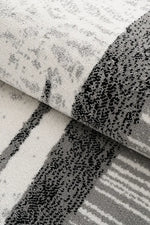 A close-up of a folded area rug showing its textured pattern, featuring a mix of distressed gray and black motifs on a white background.