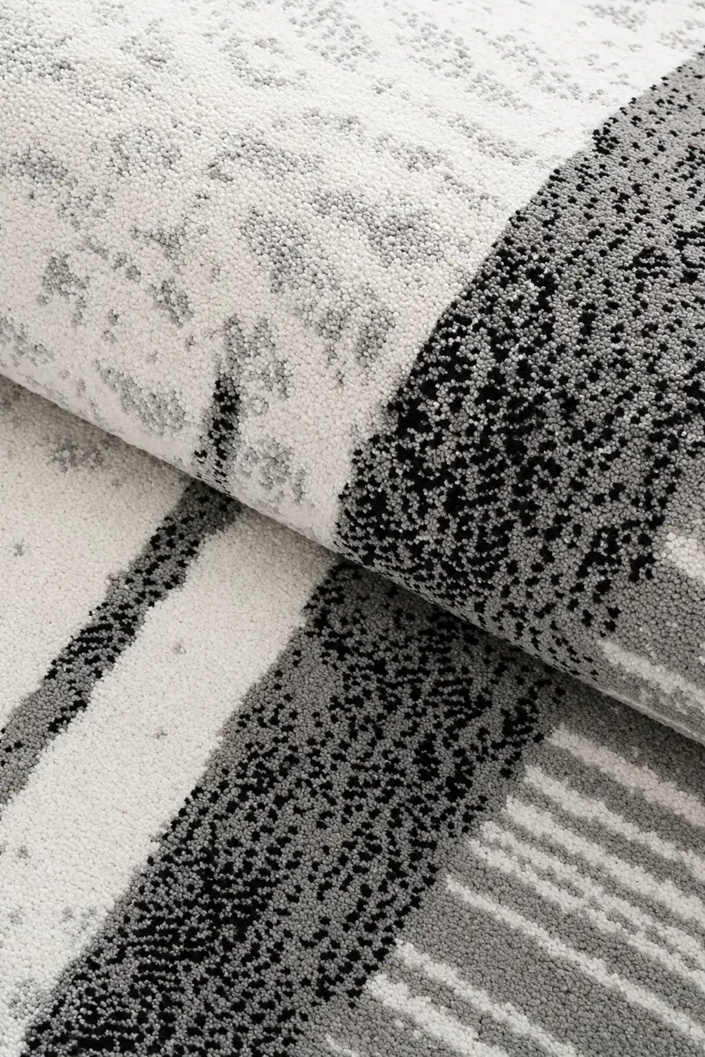 A close-up of a folded area rug showing its textured pattern, featuring a mix of distressed gray and black motifs on a white background.