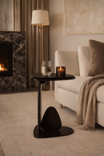 Modern living room with a black side table, candle, and glass near a fireplace.