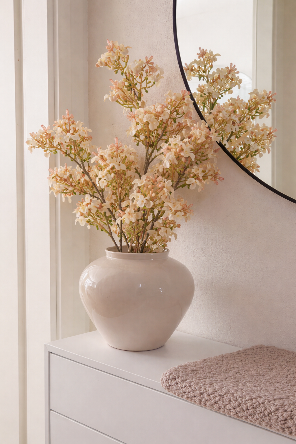 White vase with flowers on a dresser next to a mirror