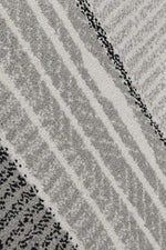 A close-up of a textured area rug featuring a modern geometric pattern of diagonal stripes and dotted lines in shades of gray, off-white, and black.