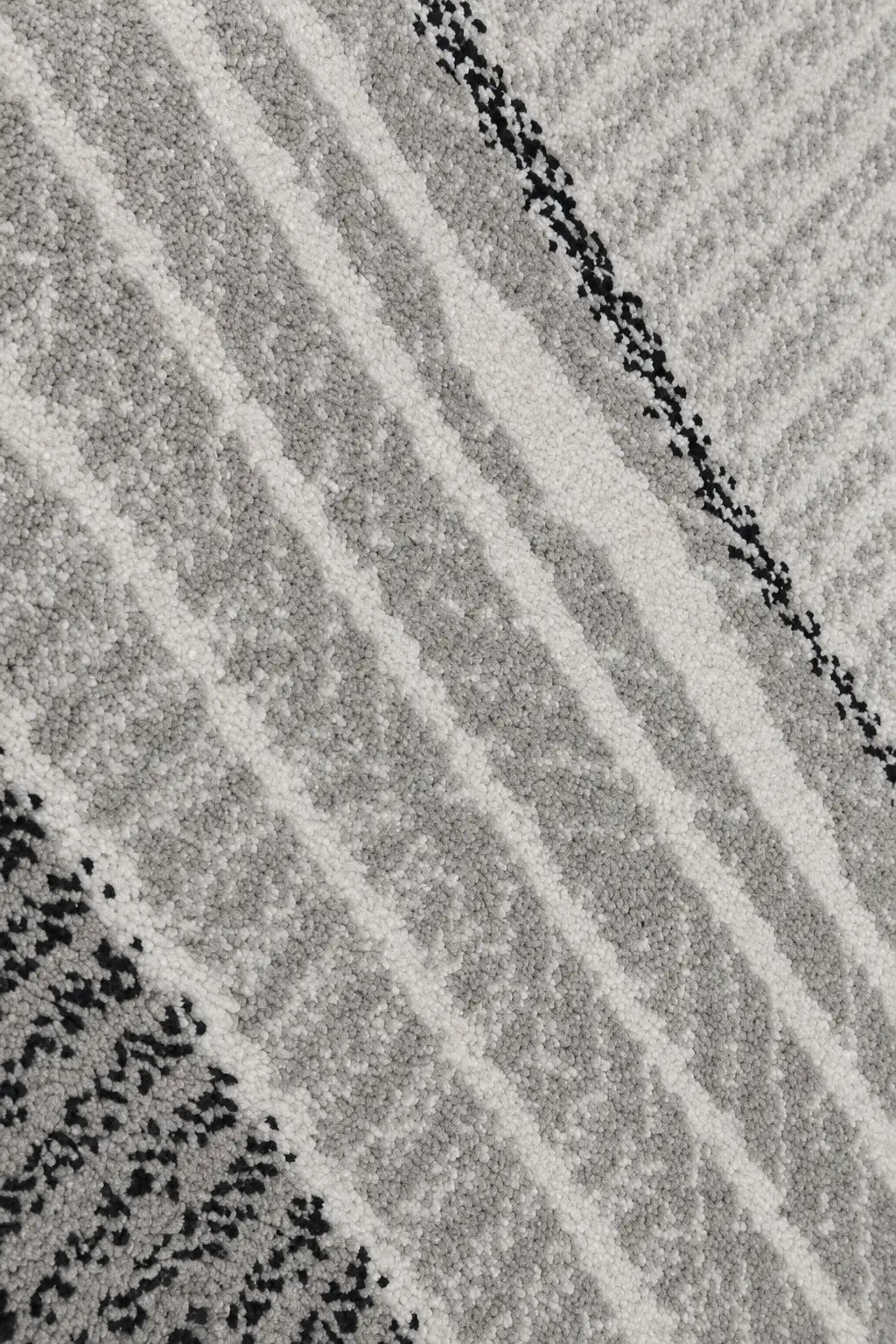 A close-up of a textured area rug featuring a modern geometric pattern of diagonal stripes and dotted lines in shades of gray, off-white, and black.