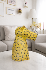 Yellow floral-patterned dress on a mannequin in a living room setting with a Prada sign in the background.