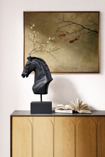 Decorative black horse head sculpture on a wooden cabinet with a framed painting in the background.