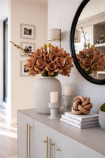 Decorative setup with a vase of flowers, candles, and books on a cabinet.